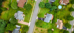 Aerial view of a suburban neighbourhood with houses, driveways, lawns, trees, and a street running through the centre, resembling the organised layout of a PLC Header.