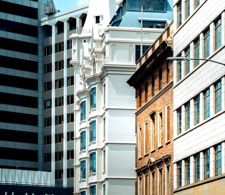 Several multi-storey buildings with different architectural styles, including modern glass, ornate white, and red brick façades, are closely situated in a cityscape under a clear blue sky—an ideal setting for commercial letting and business transactions within the vibrant urban landscape.