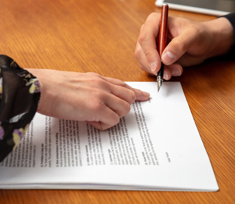 Two people at a table; one person points to a section on a printed document outlining Separation Agreements, while the other prepares to sign with a pen—both carefully reviewing their Relationship Property arrangements.