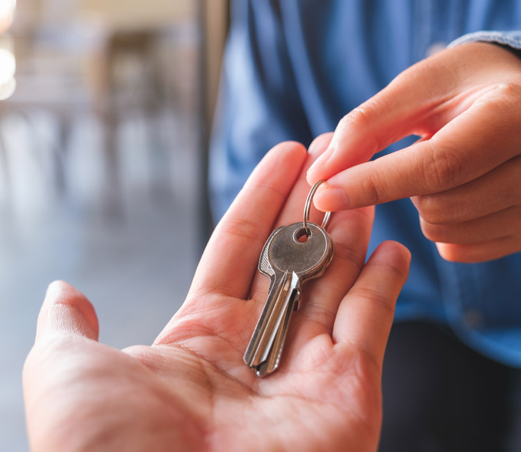 A person hands over a set of two silver keys on a keyring to another person, whose open palm is ready to receive them—symbolising the transfer of trust in important estate matters. Both individuals are visible from the wrist down.