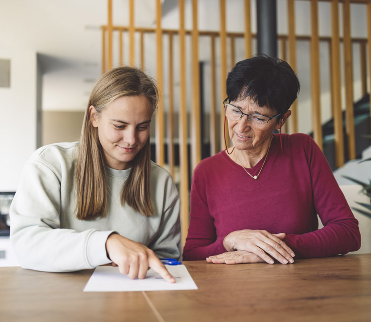 A young woman points at a document on a table while an older woman with glasses sits beside her, watching attentively. They appear to be having a focused discussion about Enduring Powers of Attorney in a modern, well-lit room.