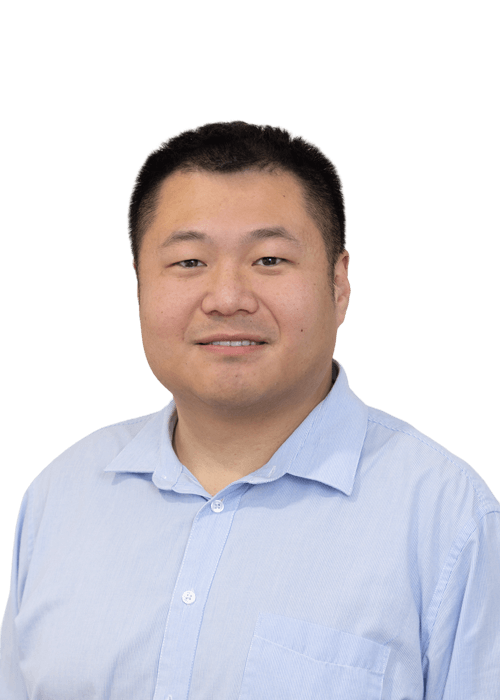 A man with short black hair is wearing a light blue button-up shirt and smiling slightly. He is facing the camera against a plain white background.